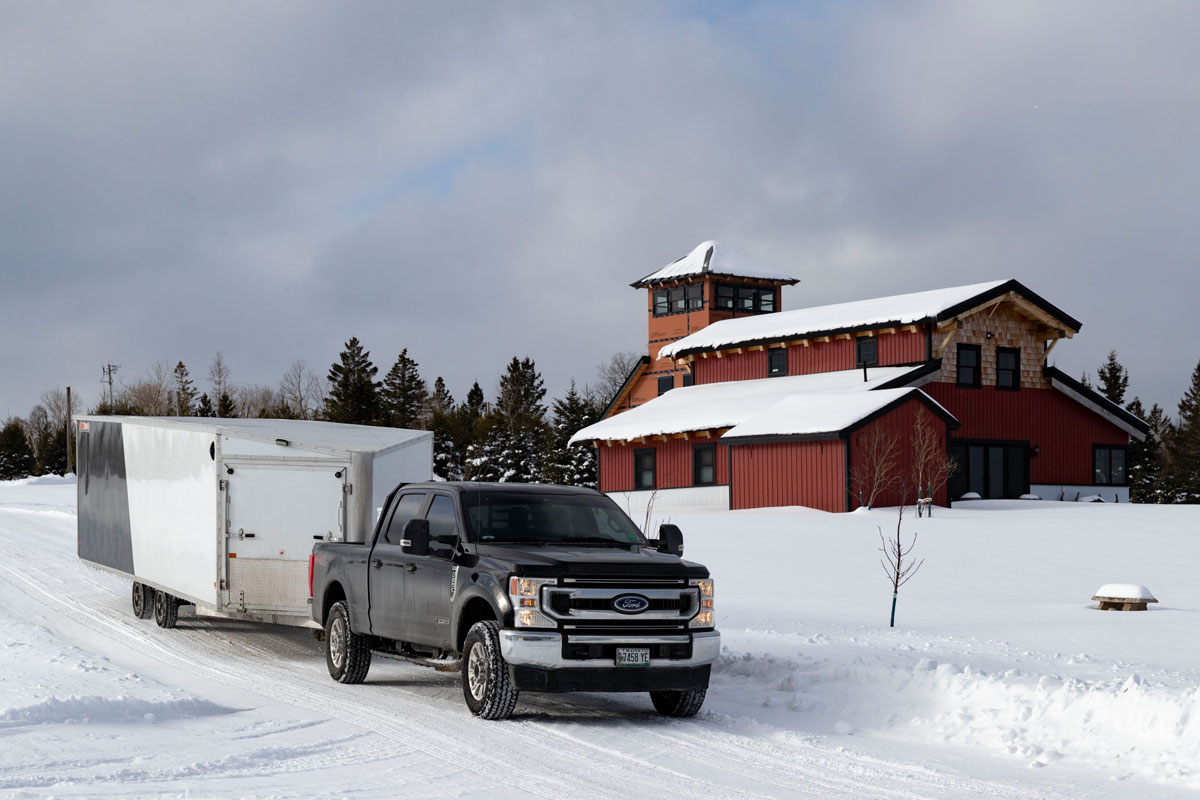 SnoPro Enclosed Deckover 6.5-Height Snow Trailers Attached To Truck With Cabins In Background