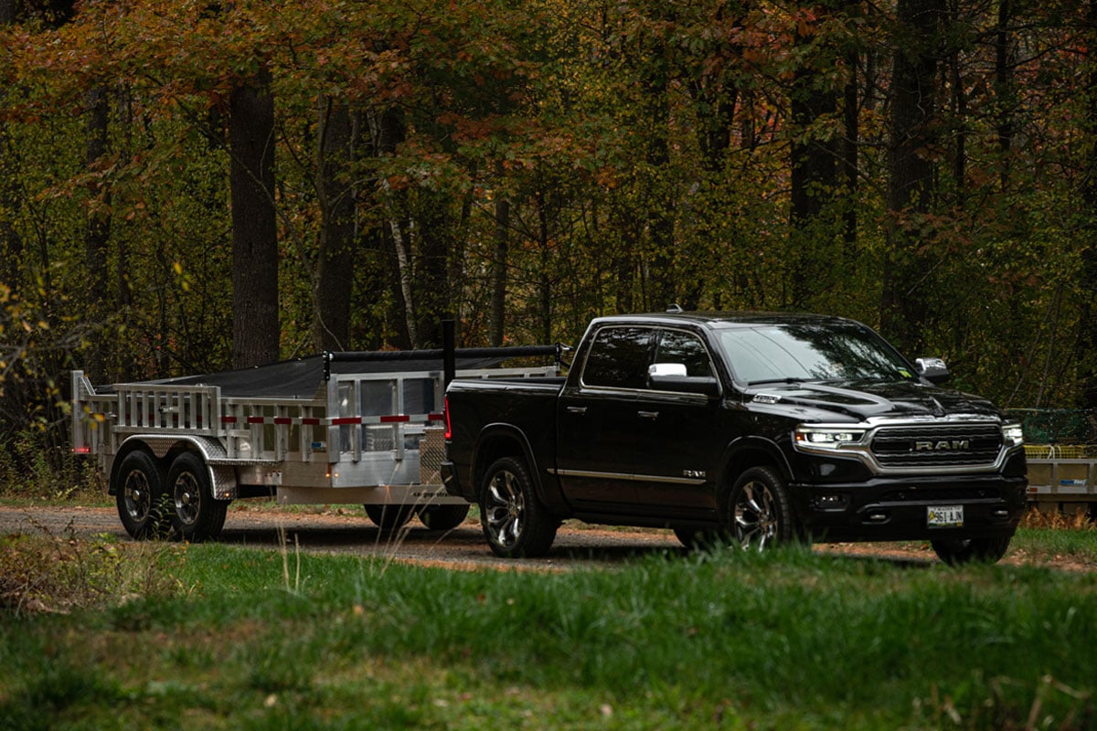 Black Truck Hauling Commercial Utility Dump Trailer Through Woods